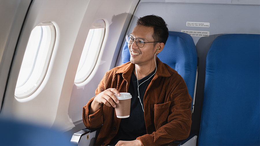 Man sitting in a luxury aircraft with a coffee and looking out the window whist smiling