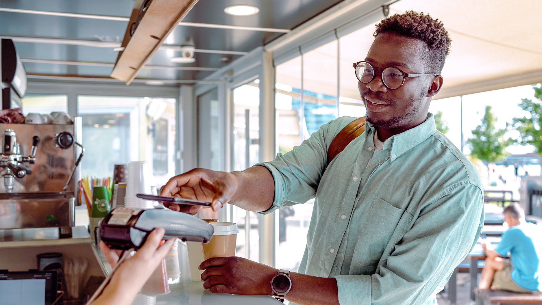 Man making a coffee purchase in a bright cafe using his Contactless phone