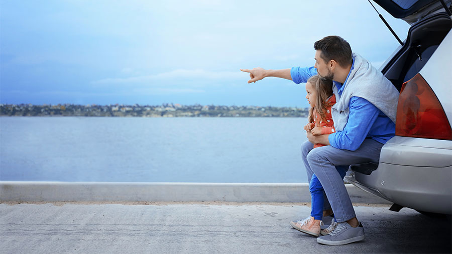 Father and daughter looking at a river while sitting on the car