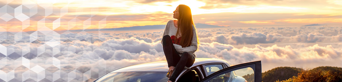 Woman sitting on car looking at sunset.