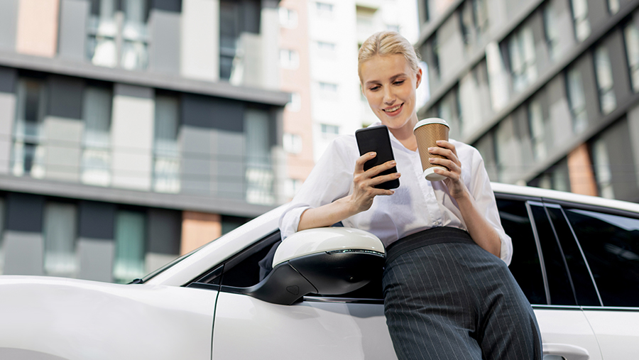 Woman leaning on car with coffee and phone